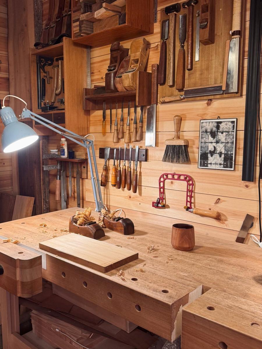 Rafael's workbench under a lamp, with wooden planes on it and the tool wall behind