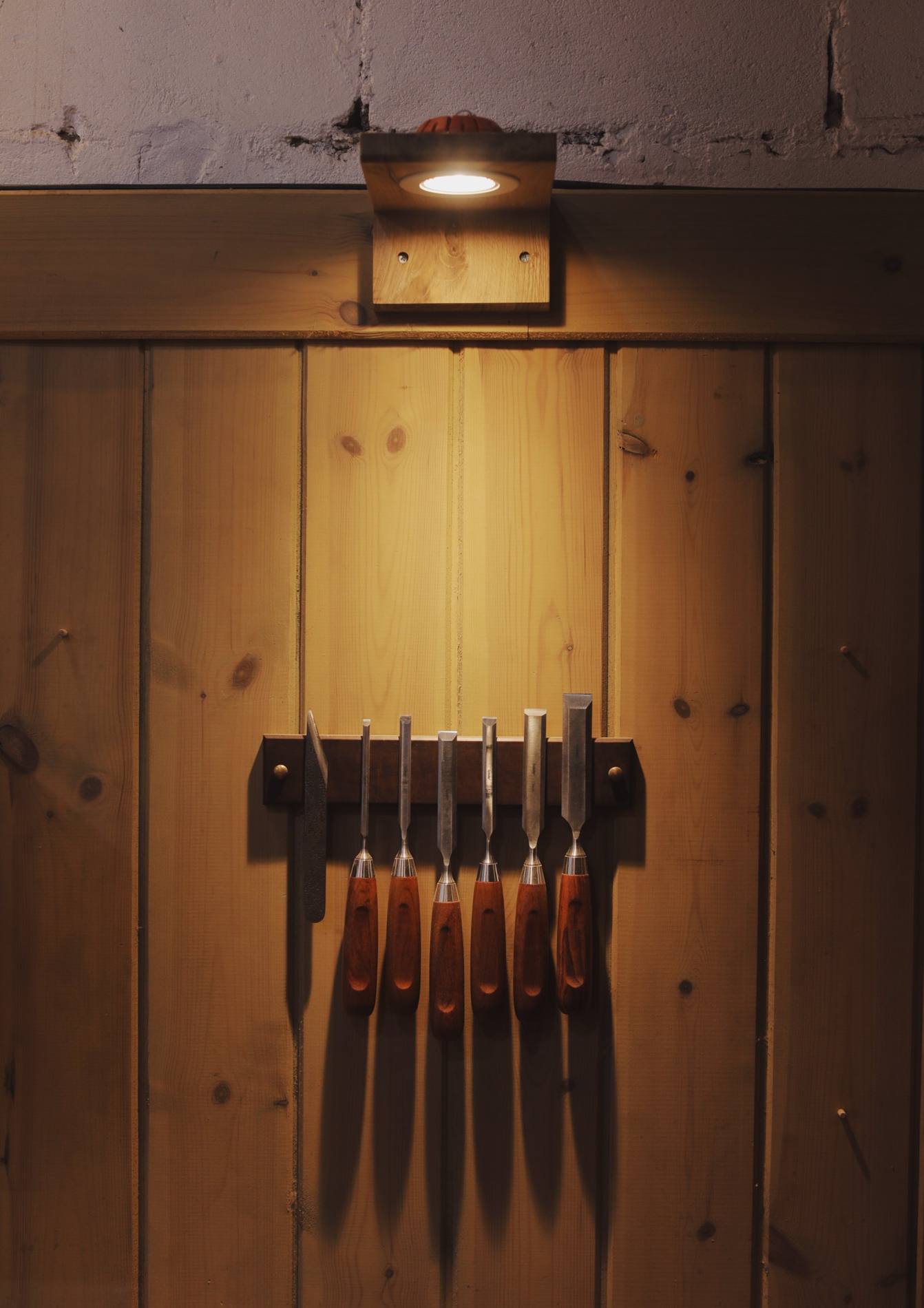 Chisels hanging on the workshop wall, under a small lamp