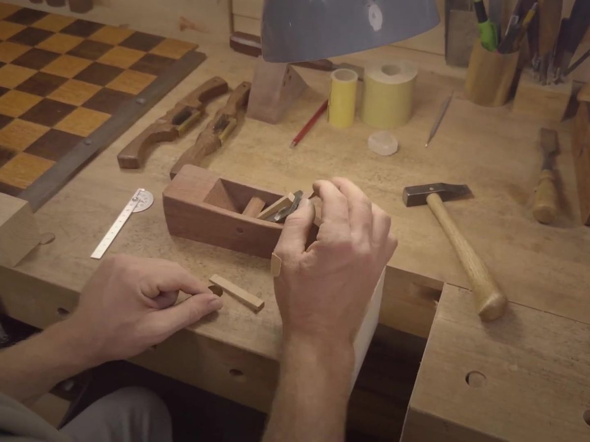 Rafael setting a wooden plane at the bench, a small hammer lying beside it